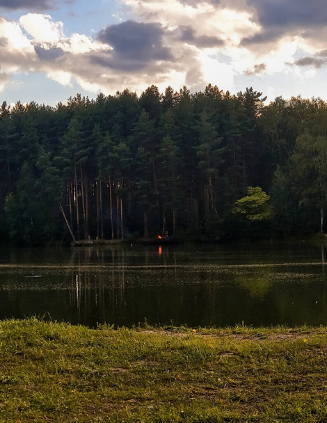 View of a gloomy coniferous summer forest located across the river, and a bonfire on the other bank, Nizhny Novgorod region, 2019.  - Foto, imagen