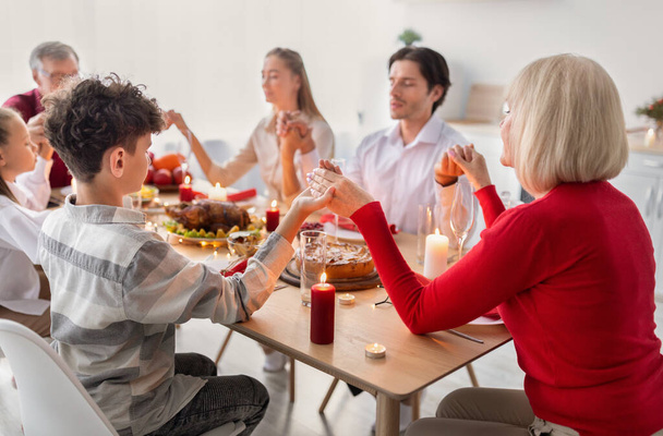 Мультипоколение семьи молятся перед праздничным обедом, держась за руки, воздавая благодарность Богу дома - Фото, изображение