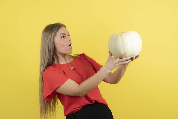 Young pretty woman wearing red t-shirt holding ripe pumpkin and posing . High quality photo - Foto, afbeelding