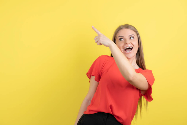 Photo of a young woman pointing up with finger against yellow wall . High quality photo - Φωτογραφία, εικόνα