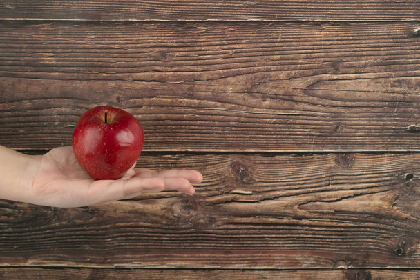 Mano femminile che tiene la mela rossa su uno sfondo di legno. Foto di alta qualità - Foto, immagini
