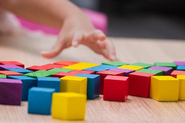 Цветной деревянный кубик на столе, детская рука играет.. - Фото, изображение