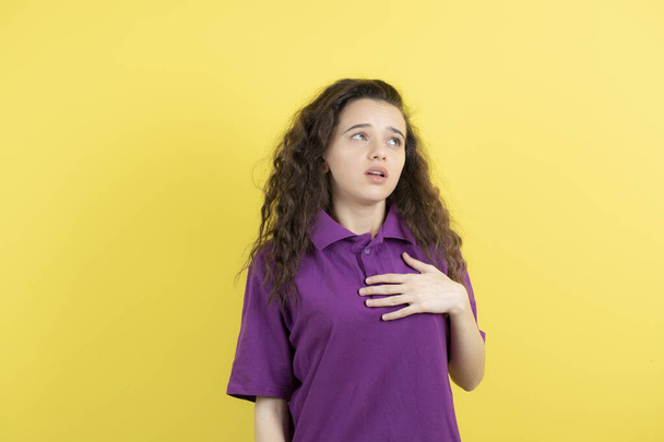 Immagine di un'adolescente riccia in t-shirt viola che si sente sopraffatta dal muro giallo. Foto di alta qualità - Foto, immagini