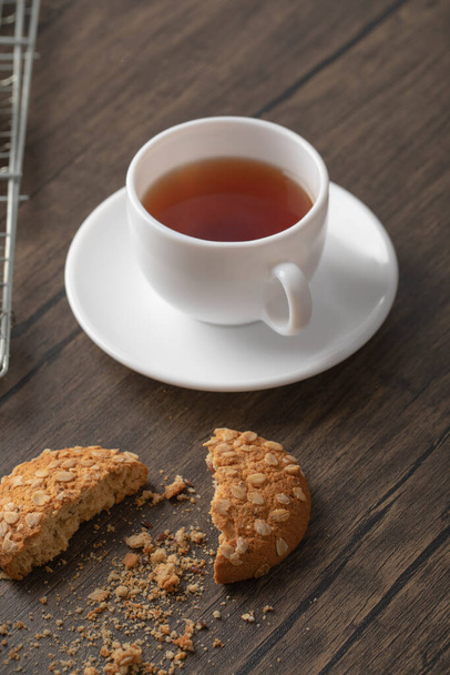 Biscotti di farina d'avena con semi e cereali vicino a una tazza bianca di tè nero. Foto di alta qualità - Foto, immagini