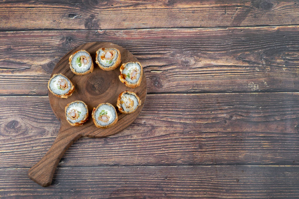 Drewniana deska sushi bułki z krewetkami, awokado, ser, omlet panierowanie. Wysokiej jakości zdjęcie - Zdjęcie, obraz