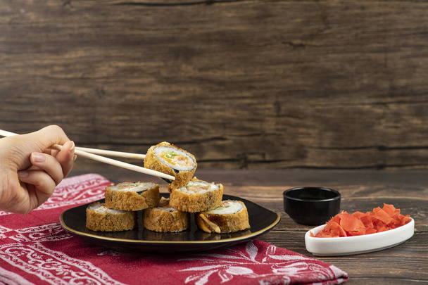 Mano femenina tomando rollo de sushi caliente con palillos en superficie de madera. Foto de alta calidad - Foto, imagen