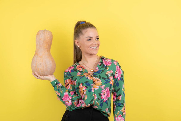 Obrázek ženy držící čerstvou dýni z máslového ořechu u žluté stěny. Kvalitní fotografie - Fotografie, Obrázek