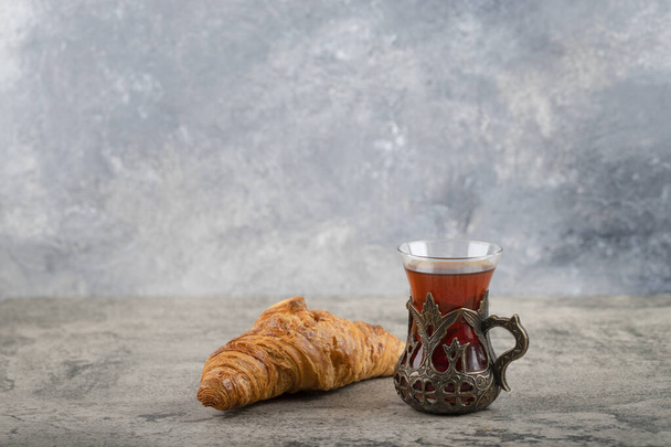 石のテーブルの上に置かれたお茶のコップが付いている1つの全体おいしいバタークロワッサン。高品質の写真 - 写真・画像