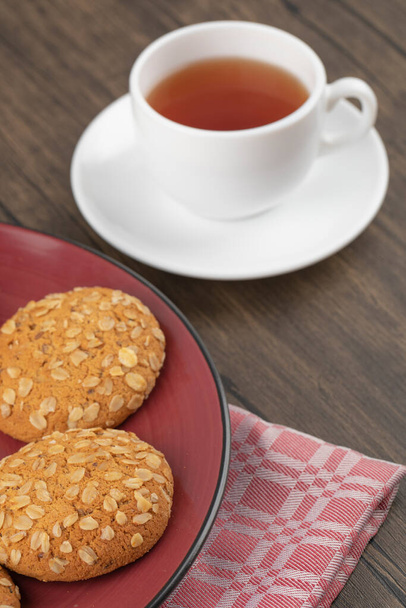 Piatto rosso con biscotti di farina d'avena e tazze di tè caldo sul tavolo di legno. Foto di alta qualità - Foto, immagini