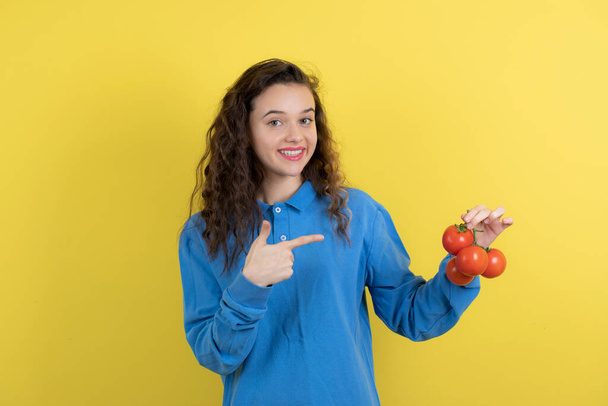 Jong tienermeisje in blauw sweatshirt met verse tomaten en staande. Hoge kwaliteit foto - Foto, afbeelding