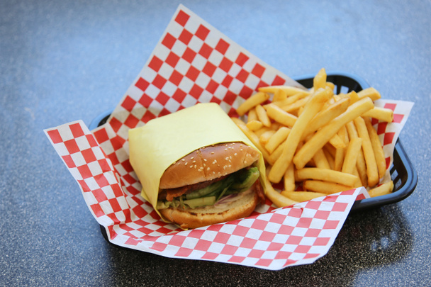 Sajtburger sült krumplival. Ebéd Friss Grillezett Sajt Burger és sült krumpli egy piros-fehér ellenőrző helyen szőnyeg egy gyorsétterem. Mindenki szereti a sajtburgert és a sült krumplit ebédre. - Fotó, kép