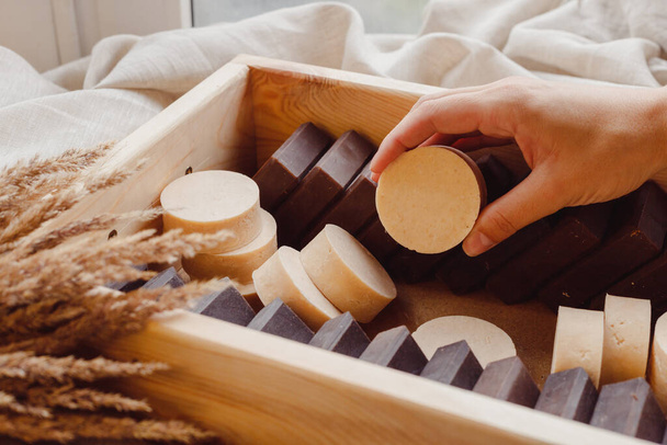 Рука бере саморобне мило з дерев'яної коробки, наповненої натуральним твердим шмпо та милом. Контроль якості, доставка, партія
 - Фото, зображення