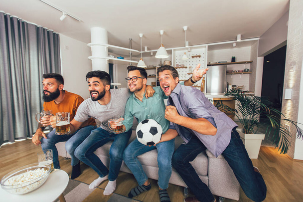 Happy male friends or football fans watching soccer on tv and celebrating victory at home. - Foto, Imagen