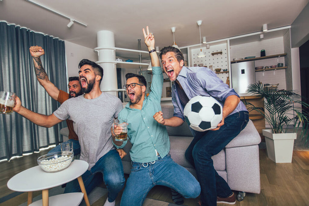 Happy male friends or football fans watching soccer on tv and celebrating victory at home. - Photo, Image