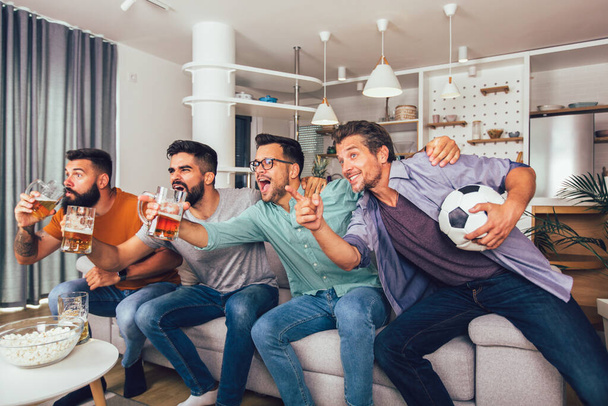 Szczęśliwy mężczyzna przyjaciele lub kibice piłki nożnej oglądając piłkę nożną w telewizji i świętując zwycięstwo w domu. - Zdjęcie, obraz