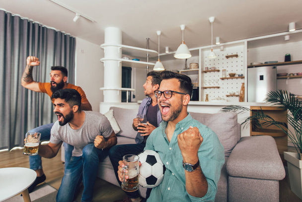 Amigos varones felices o aficionados al fútbol viendo fútbol en la televisión y celebrando la victoria en casa. - Foto, Imagen