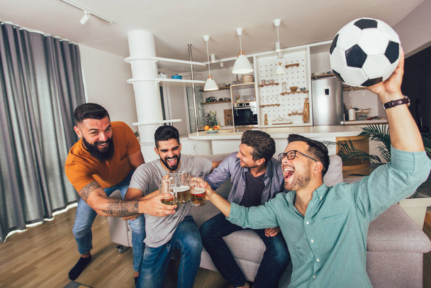 Счастливые друзья или футбольные болельщики смотрят футбол по телевизору и празднуют победу дома. - Фото, изображение