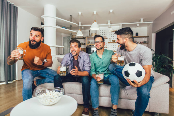 Hombres viendo deporte en la televisión juntos en casa gritando alegres. Grupo de amigos sentados en el sofá y viendo un partido de fútbol. - Foto, imagen