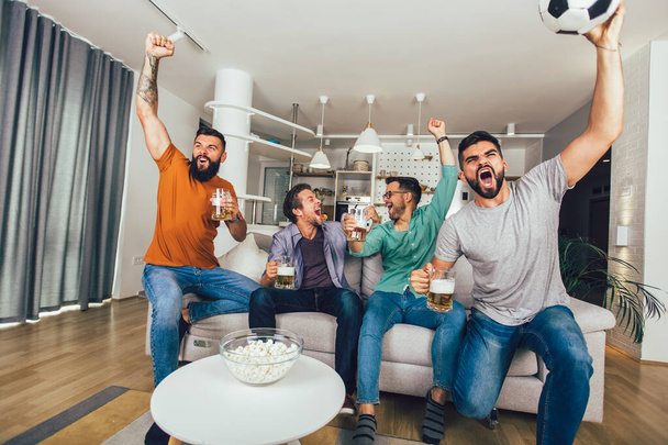 Hombres viendo deporte en la televisión juntos en casa gritando alegres. Grupo de amigos sentados en el sofá y viendo un partido de fútbol. - Foto, Imagen