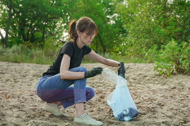 Жінка збирає сміття у мішку для сміття. Концепція планети без сміття. Очищення природи, волонтерська екологія - зелена концепція. Навколишнє середовище забруднення пластику. Турбота про природу
 - Фото, зображення