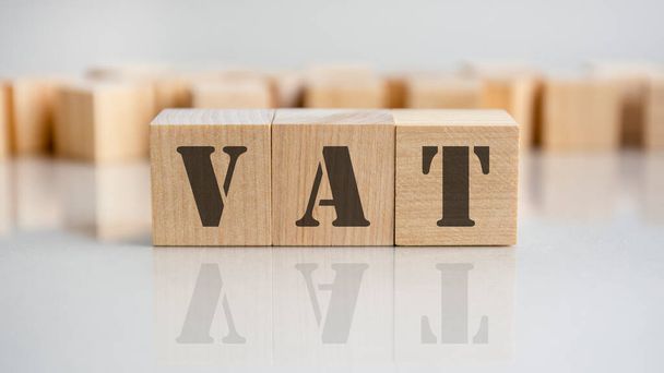 Słowo VAT napisane na drewnianym bloku. Słowo VAT składa się z drewnianych klocków leżących na szarym stole, koncepcja biznesu. - Zdjęcie, obraz