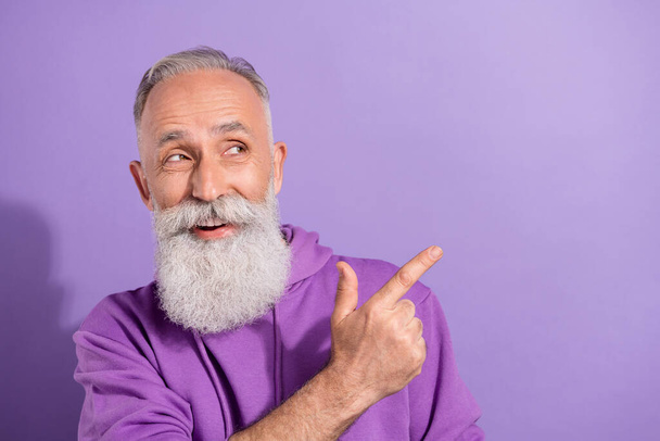 Portrait of attractive elderly retired cheerful grey-haired man demonstrating copy space offer isolated over purple violet color background - Foto, imagen
