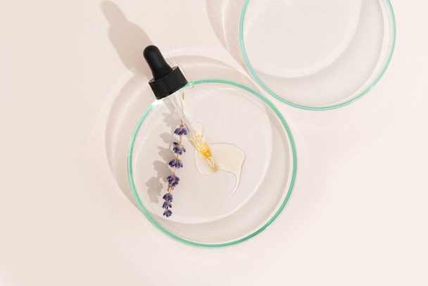 Cosmetisch pipetserum op een petrischaal van lichte lavendelkleur op een beige achtergrond. Cosmetologie, farmaceutica. Zure peeling, gezichtsolie, collageen - Foto, afbeelding