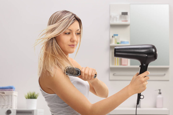 Young woman using a hairbrush and a blowdrying hair in a bathroom  - Foto, Bild