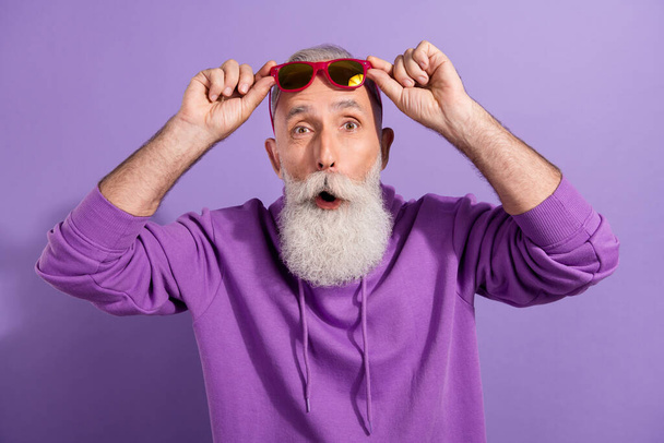 Portrait of elderly funky amazed hipster grey-haired man touching specs news reaction isolated over purple violet color background - Foto, imagen
