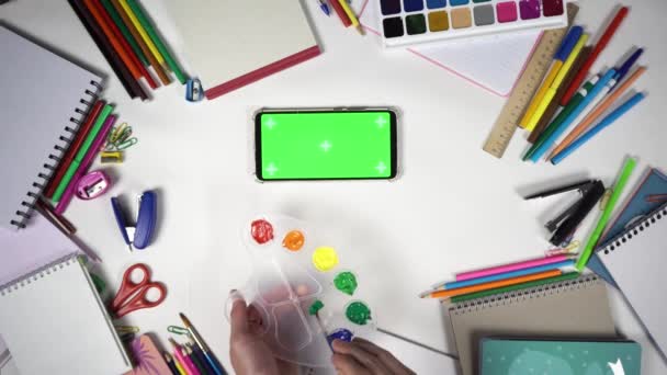 Człowiek uczy się rysować za pomocą palety kolorów i pędzlem oglądając lekcje online na smartfonie - Materiał filmowy, wideo