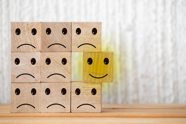 wooden cubes with smiling emoticons and sad one on wood table, blue background. Space for text. emotional state concept - Photo, Image