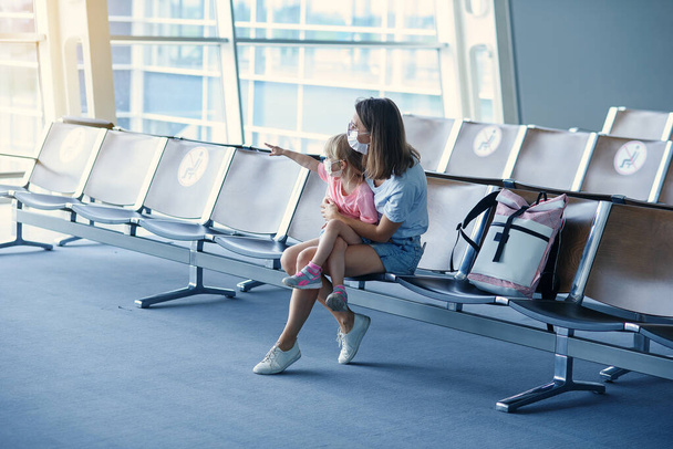 Mãe com filha em máscaras à espera do voo no aeroporto. Mulher com menina no aeroporto internacional. - Foto, Imagem