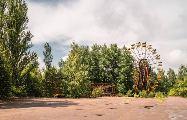 Panorama view of abandoned rides and ferris wheel in the decaying amusement park of Pripyat, Ukraine inside the Chernobyl Exclusion Zone - Photo, Image