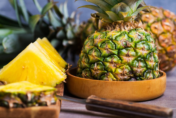 Slices and half of ripe pineapple close-up. Wooden bowl and cutting board with a knife. - Fotó, kép