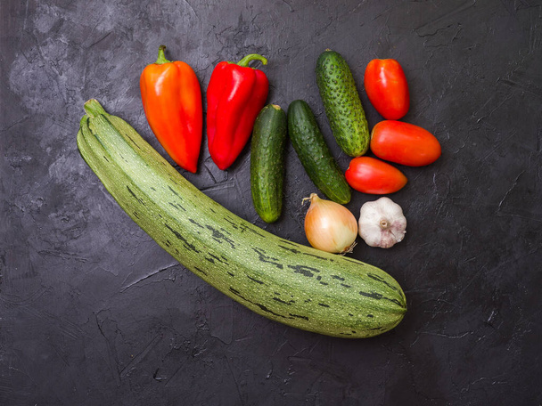 Vegetables on a black background. Ingredients for a vegetarian meal. Zucchini, red bell peppers, onions, garlic and cucumbers. View from above - Foto, imagen