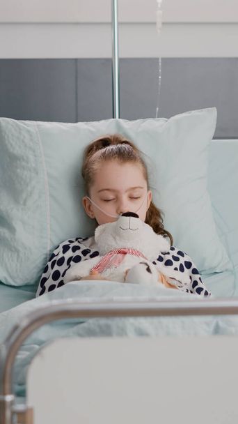 Porträt eines kranken Kindes im Krankenhaus, das einschläft, während es Teddybär in den Händen hält - Foto, Bild