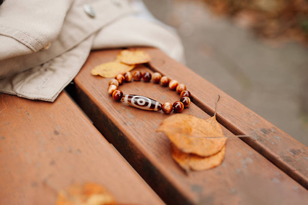 Tibetan talisman bracelet with minerals and magic dzi bead to attract good luck in life. energy trappings. autumn still life bracelet in leaves on wood. selective focus - Photo, Image