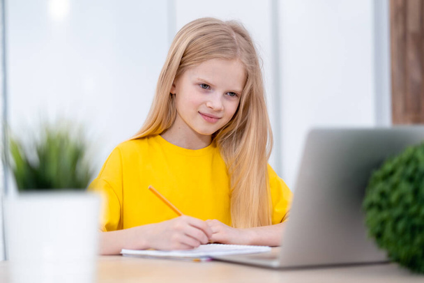 Blonde schoolgirl studying at home doing school homework with laptop. Distance learning online education. Back to school - Foto, Imagen