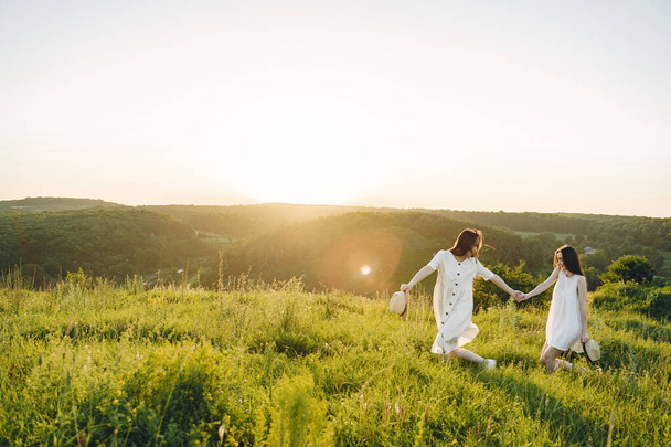 Portrait of two sisters in white dresses with long hair in a field - 写真・画像