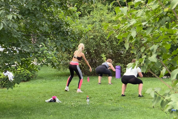 Групповые бесплатные занятия для людей разного возраста и пола в городском парке. Спорт в солнечный день летом - Фото, изображение