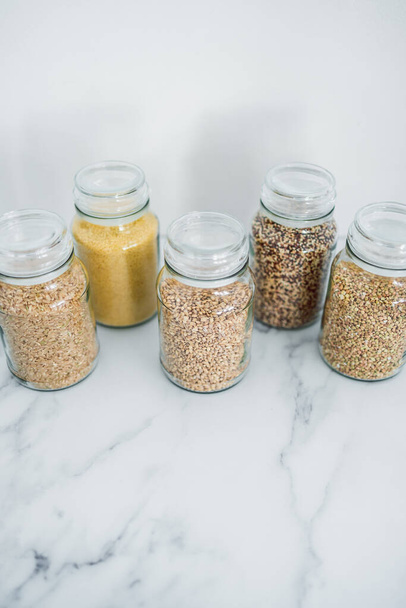 clear pantry jars with different types of grains in them including quinoa rice buckwheat couscous and barley, concept of simple natural healthy ingredients - Фото, зображення