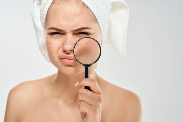 mujer con una toalla en la cabeza sosteniendo una lupa cerca del primer plano de higiene facial - Foto, imagen
