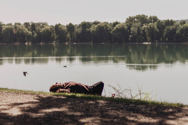 A man in a brown shirt lies on the shore of the lake - Zdjęcie, obraz