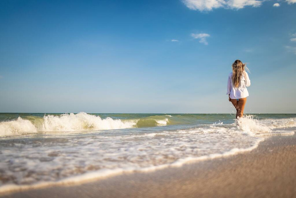 A tanned girl in a blue swimsuit and a light shirt enjoys the summer at the seaside - Fotoğraf, Görsel