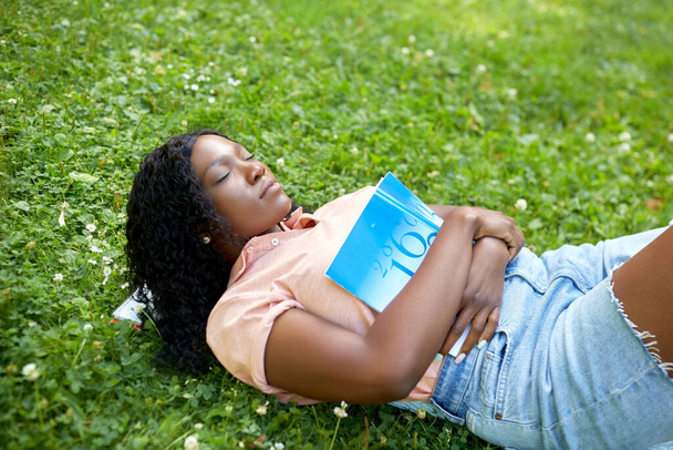 african student girl with book sleeping on grass - Fotoğraf, Görsel