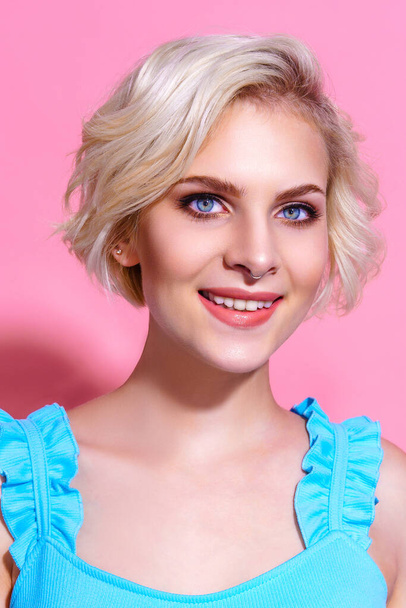 Portrait of beautiful blonde woman in blue dress posing on pink studio background - Фото, зображення