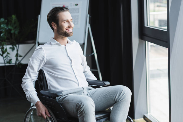 young disabled businessman in wheelchair looking away and smiling in office - Valokuva, kuva