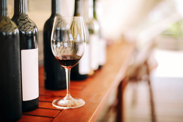 Vinné láhve a sklenice s červeným vínem na dřevěném stole na zahradním pozadí v slunečném dni party - Fotografie, Obrázek
