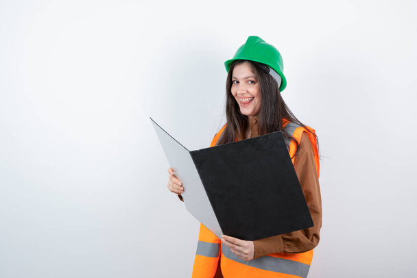 Female engineer in orange vest and green hardhat holding black clipboard . High quality photo - Foto, immagini