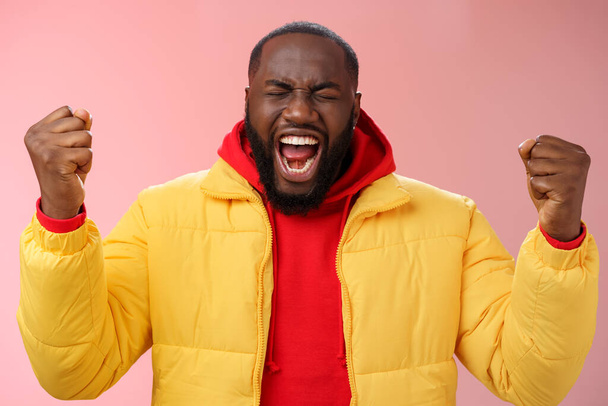 Handsome african-american man encouraging himself put will effort clenched arms yelling close eyes raise hands boost confidence, standing pink background express rage release emotions - Photo, Image